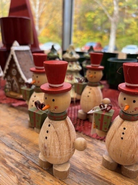 Wooden snowman figurines with red hats and gifts stand on a rustic wooden table with holiday decor.