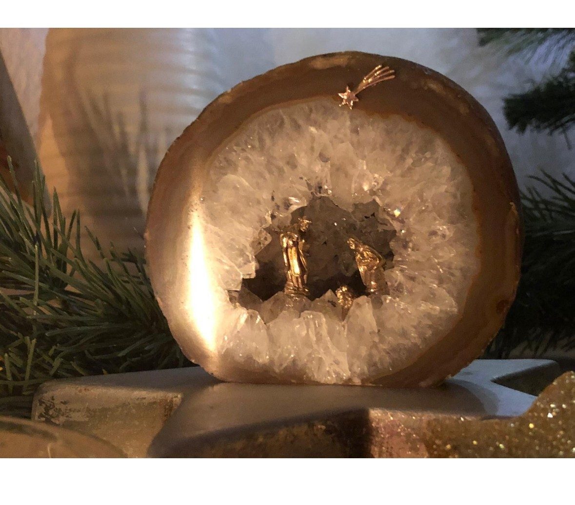 Festive geode with a golden Nativity scene inside, topped with a shooting star, beside pine.