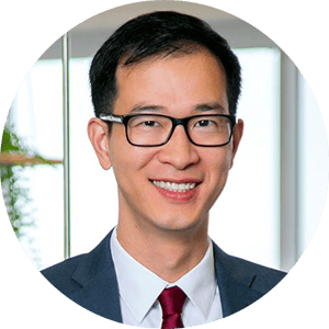 Headshot of an Asian man in a suit smiling, wearing glasses.