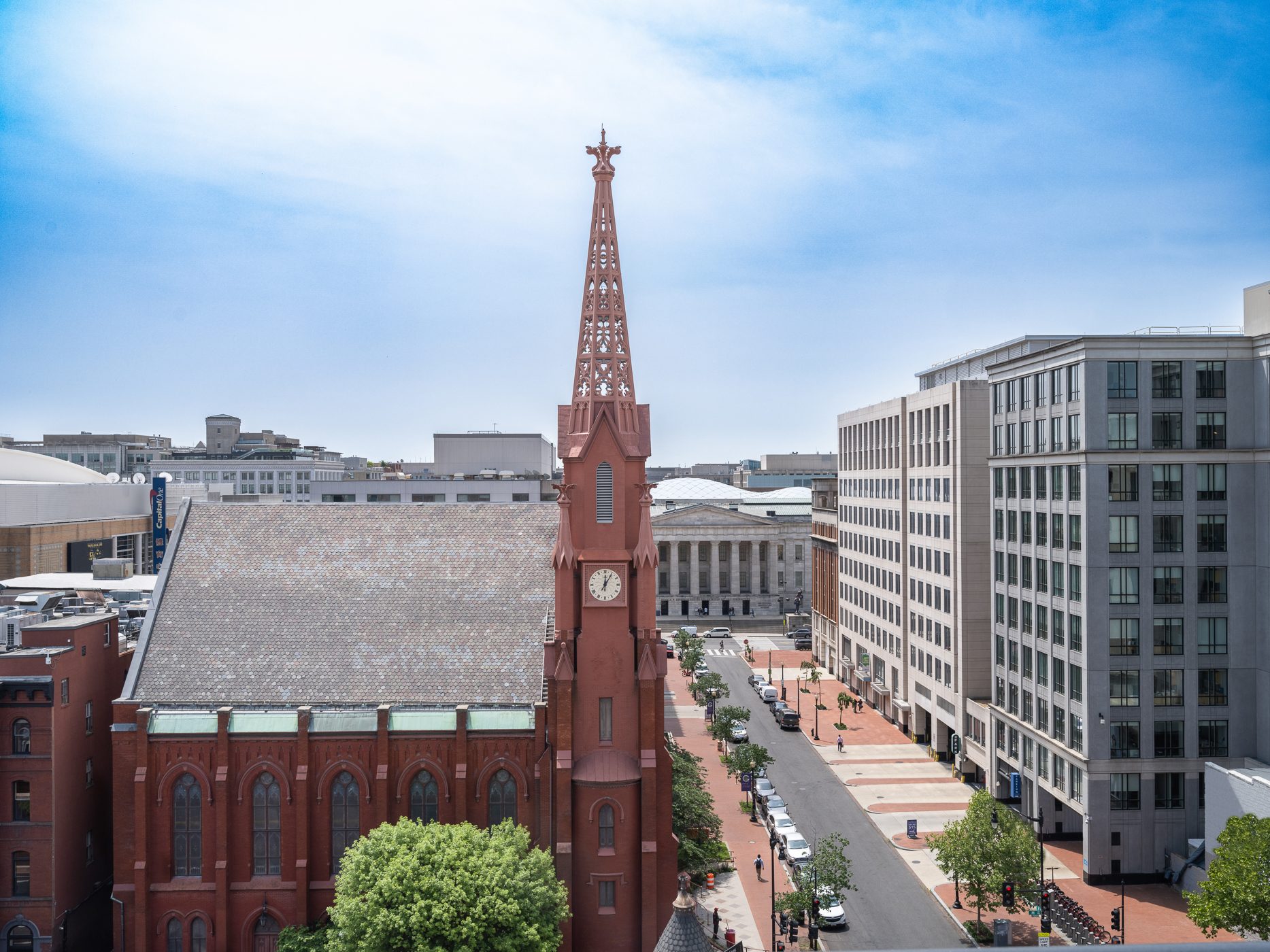 Overhead city view featuring a red church with a tall steeple, a street with cars, and modern buildings.