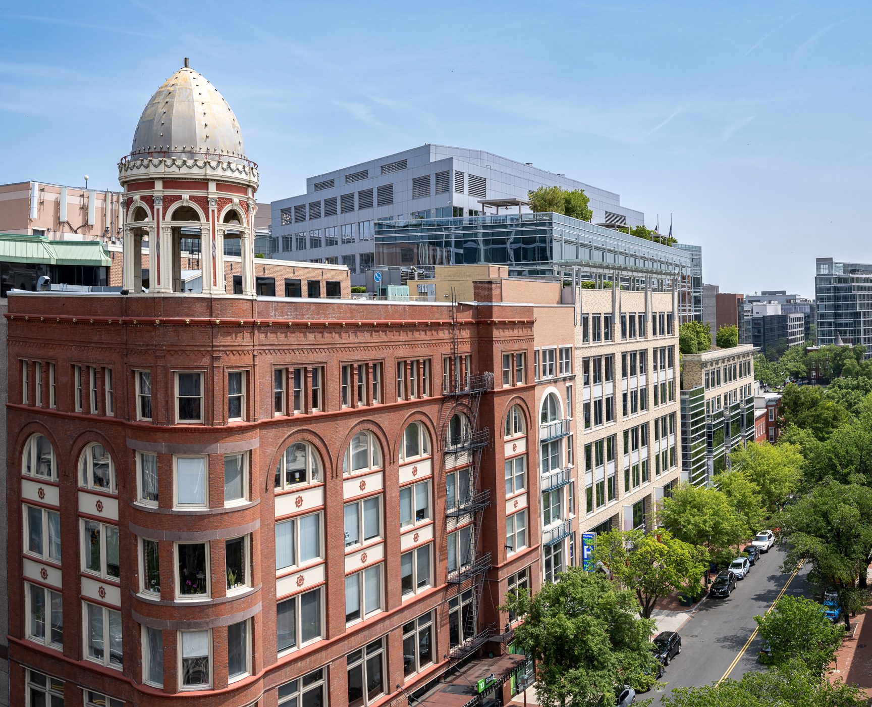 Urban view: a historic red brick building with a dome, surrounded by modern buildings and a tree-lined street.