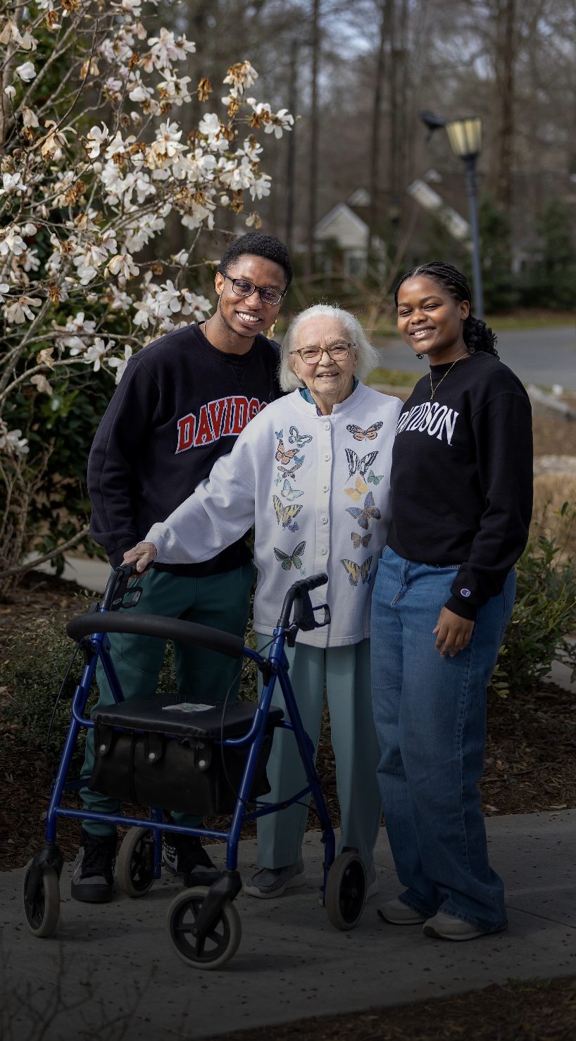 Intergenerational group: an elderly woman with a walker smiles with two young adults outdoors.