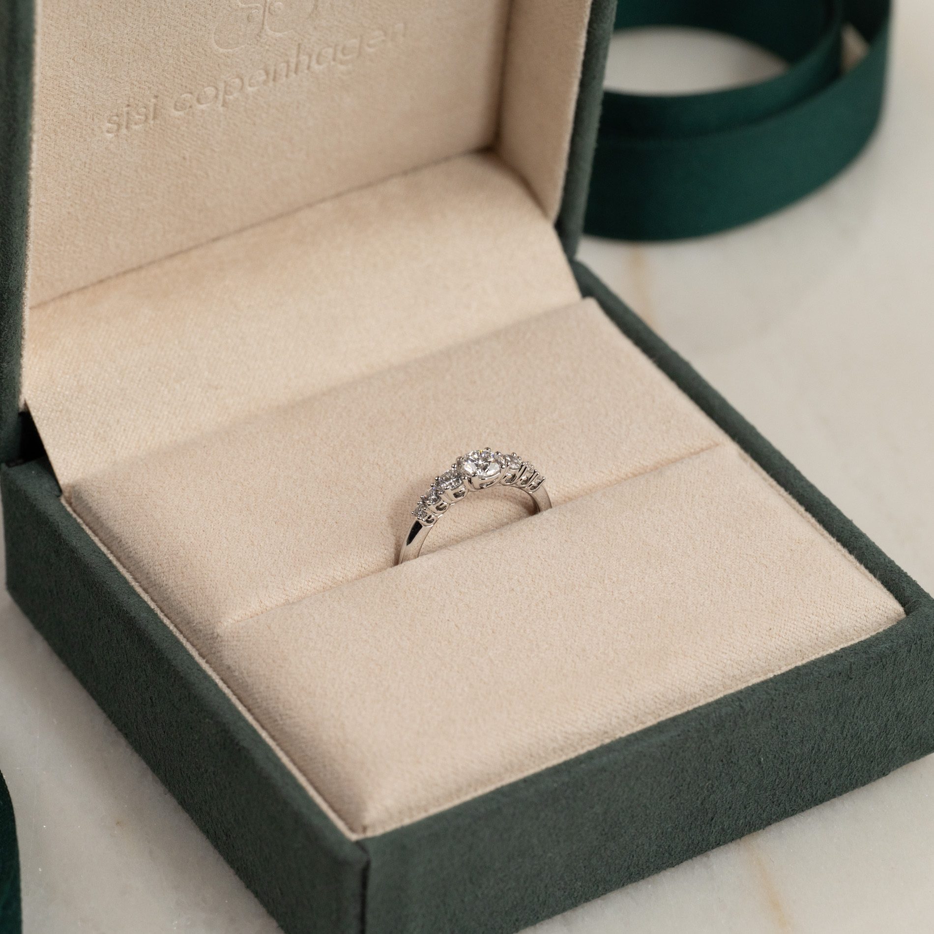 A sparkling diamond ring, featuring a prominent center stone and surrounding smaller diamonds, rests elegantly in an open green velvet jewelry box.