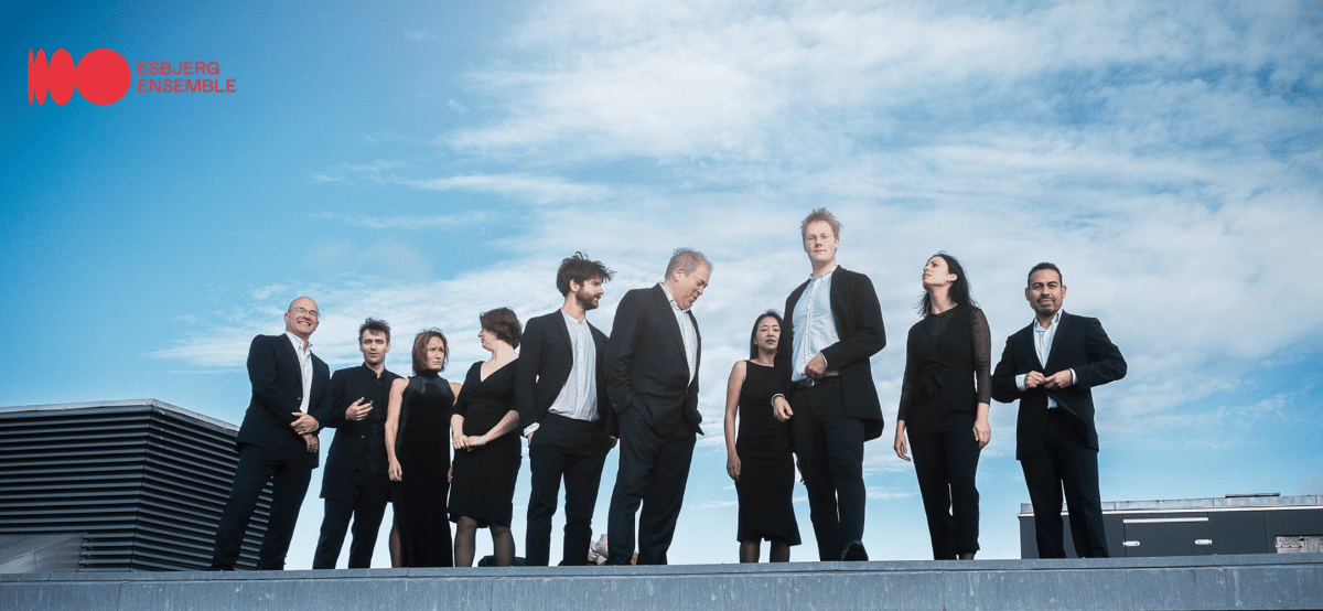 The Esbjerg Ensemble, a classical music group, posing together on a rooftop with a blue sky.