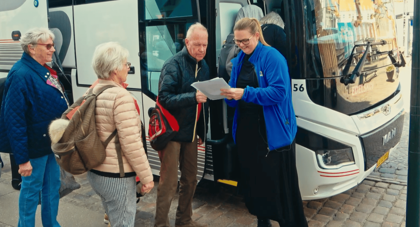 A tour guide speaks with elderly travelers next to a bus.