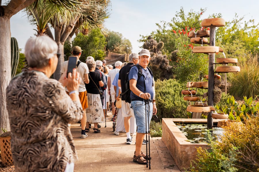 Seniors on a walking tour, a man with poles, a woman with a phone, and a tiered fountain.