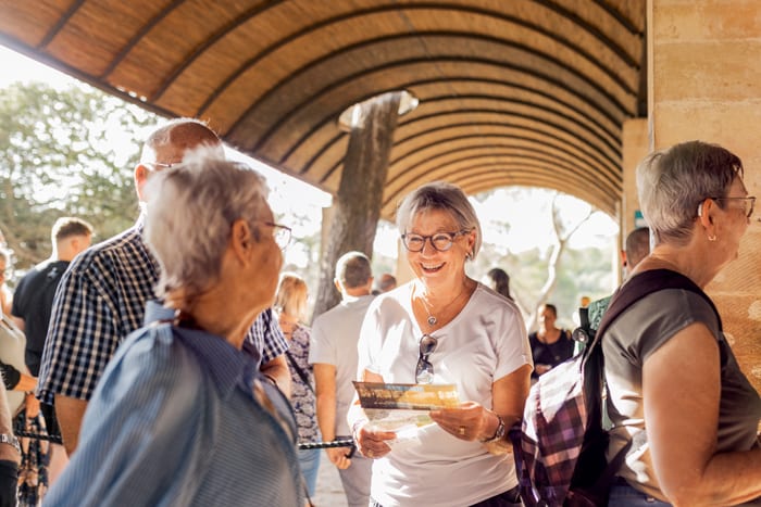 Smiling woman holds pamphlet in covered walkway with other people.