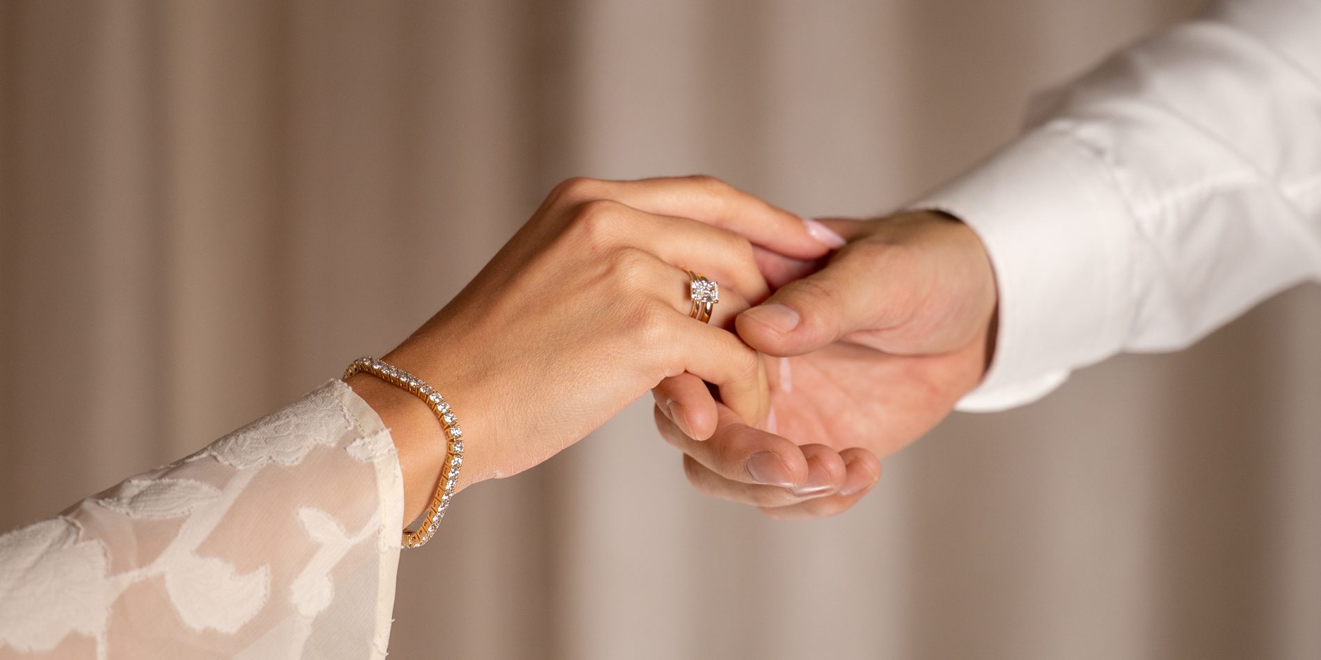 Close-up of a woman's hand with an engagement ring and diamond bracelet, held gently by a man's hand.