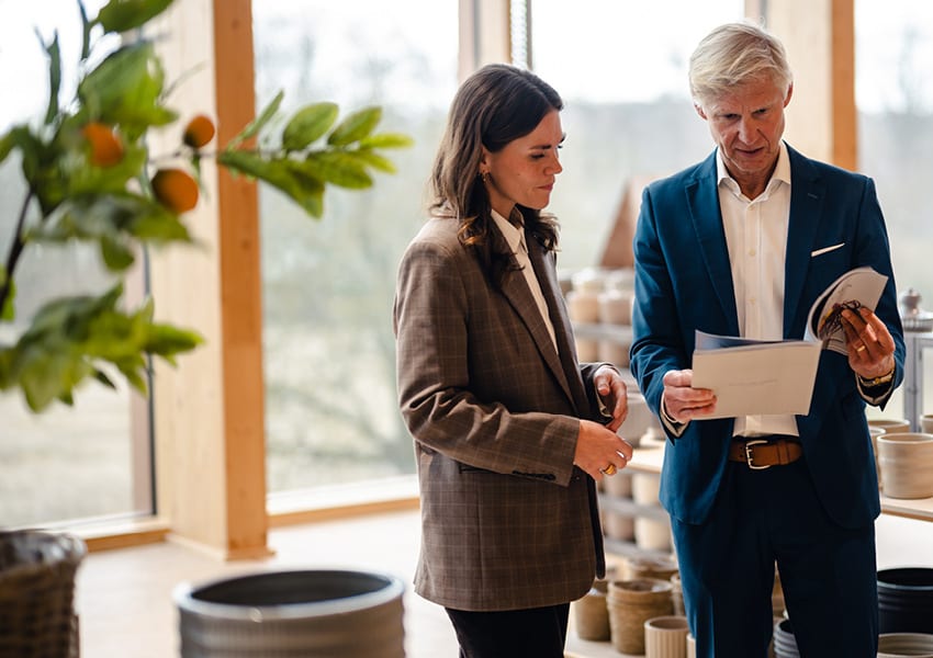Two professionals, a man and a woman, review documents in a modern, plant-filled showroom.