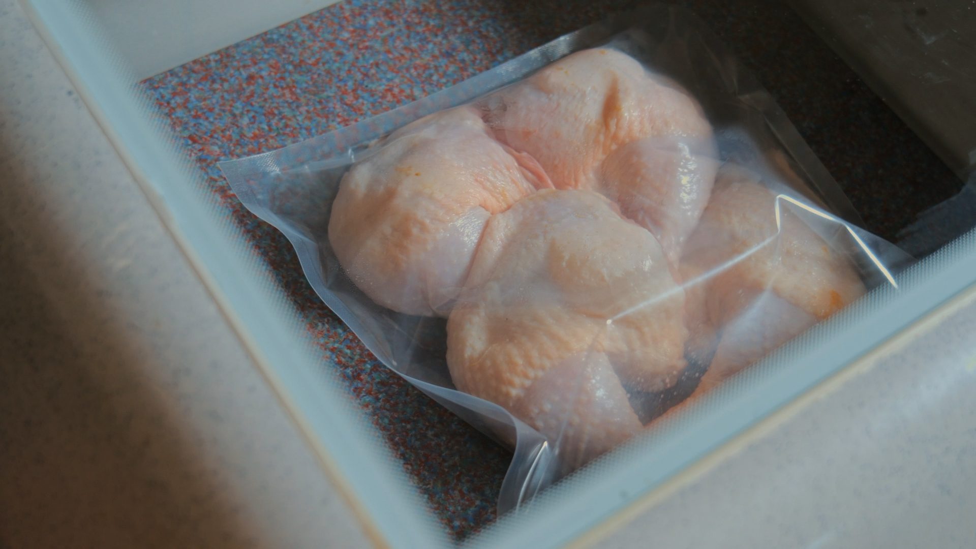 Several pieces of raw chicken, possibly breasts or thighs, in a clear vacuum-sealed bag inside a container.