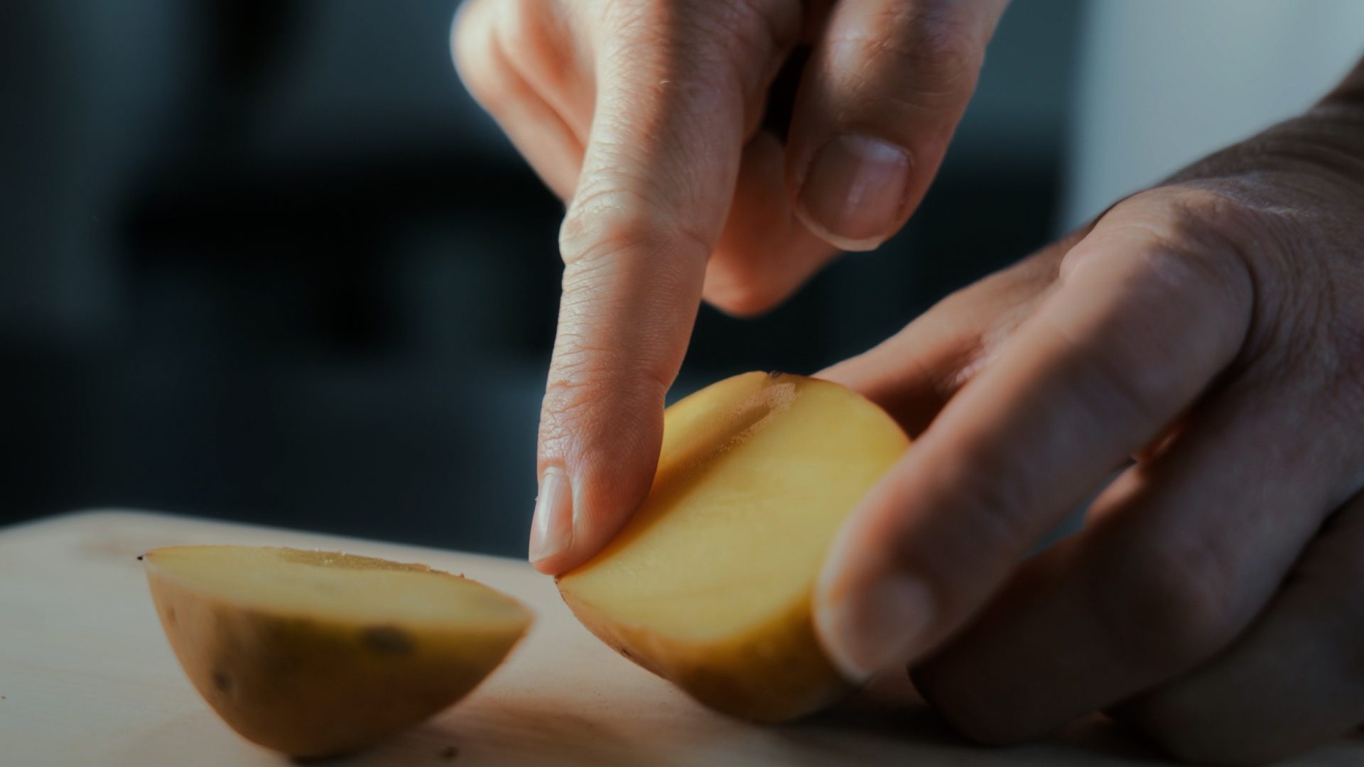 Close-up of hands preparing food, one hand holds a potato half while a finger touches its surface.