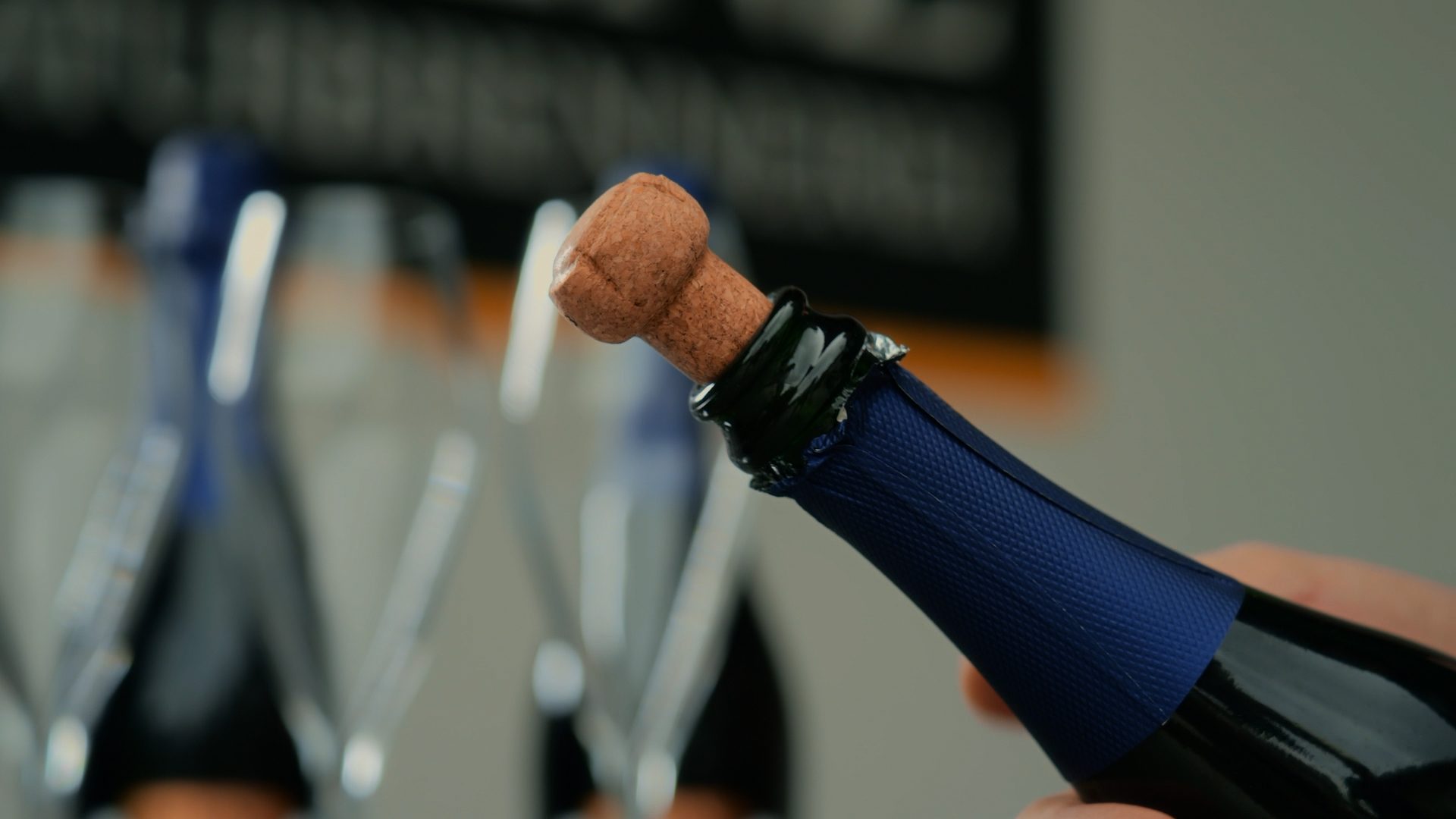 Close-up of a hand holding a champagne bottle with the cork partially out, ready to pop.