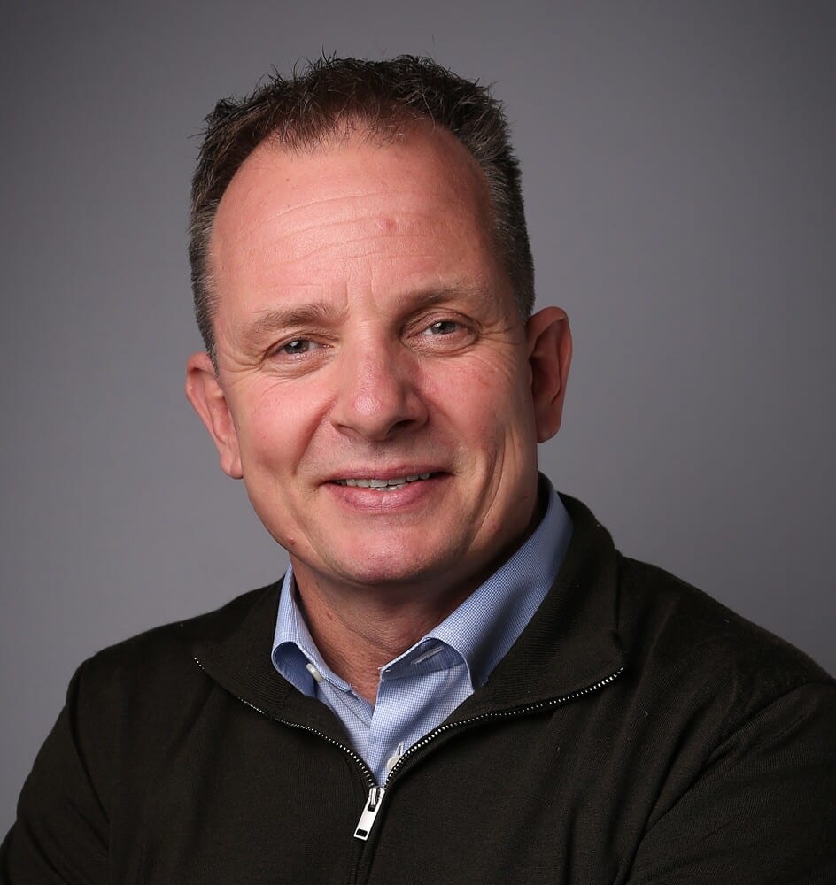 Smiling man in blue shirt and dark jacket.
