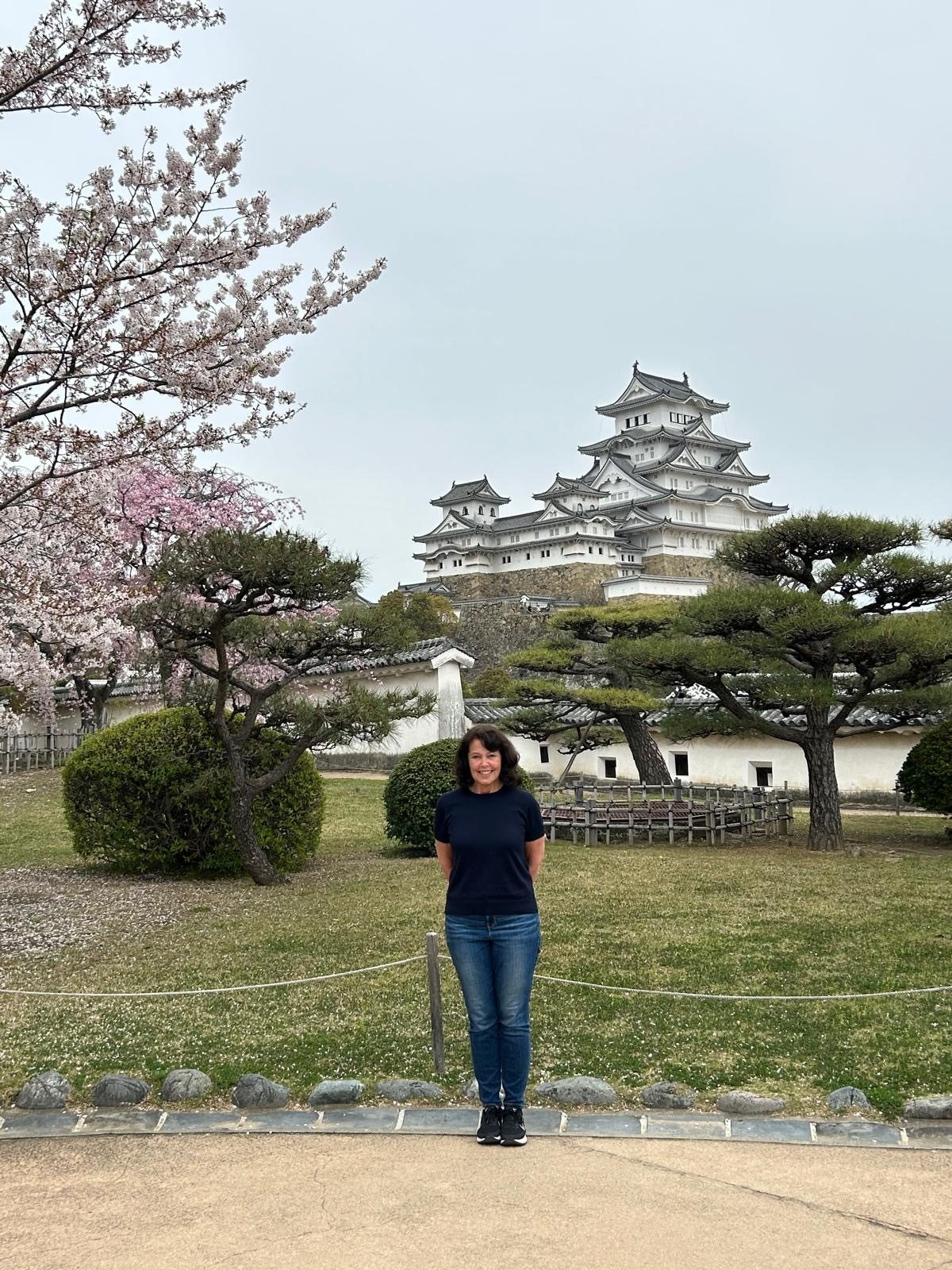 Smiling woman in a Japanese garden with Himeji Castle and cherry blossoms.