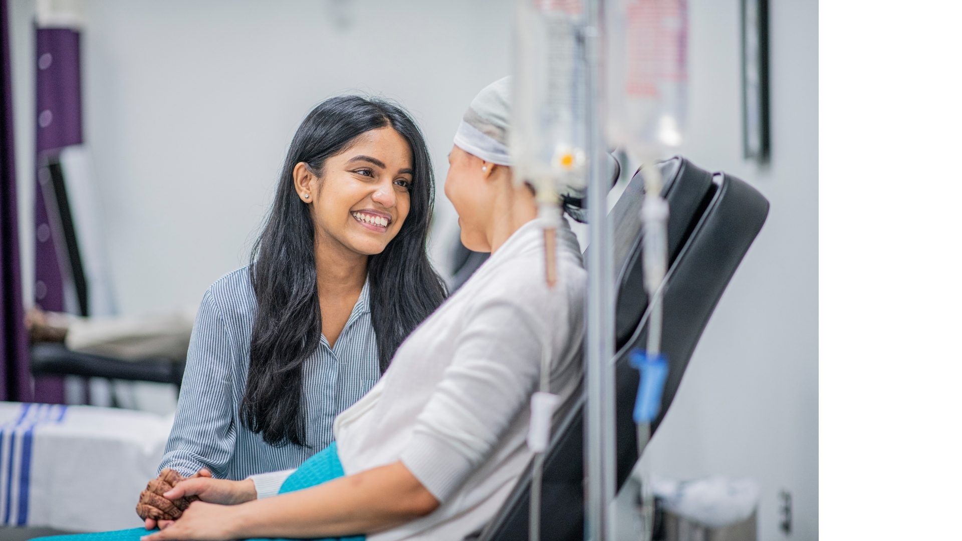 A young woman smiles warmly at a patient receiving treatment in a medical setting, offering comfort.
