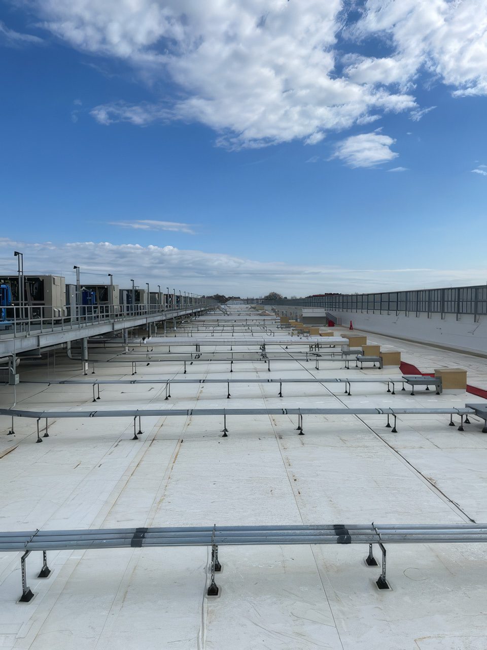 A wide shot of an industrial rooftop with extensive pipework, rows of machinery, and a vast blue sky.