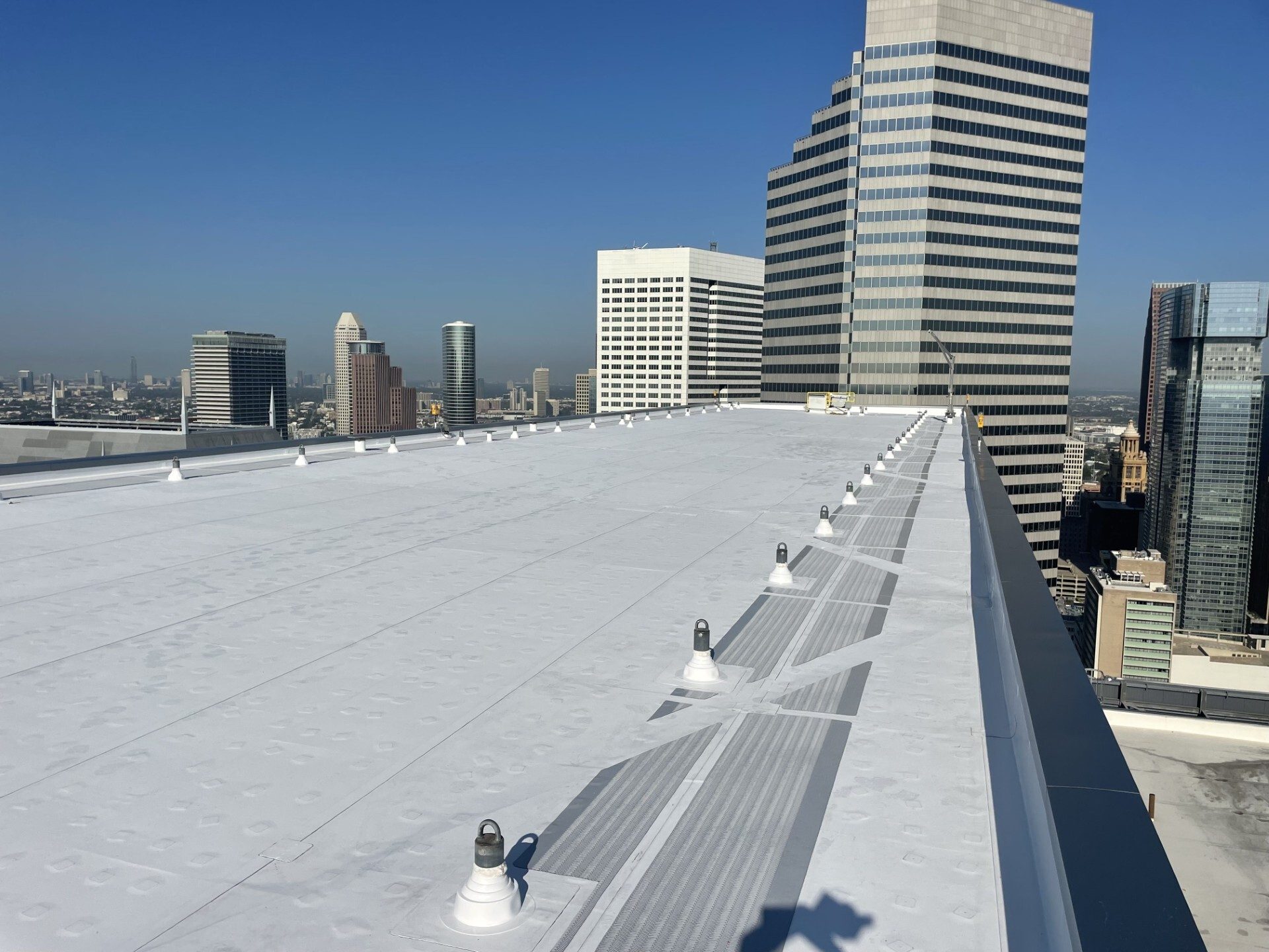 A clean white rooftop with fixtures, overlooking a city skyline with tall buildings under a clear blue sky.