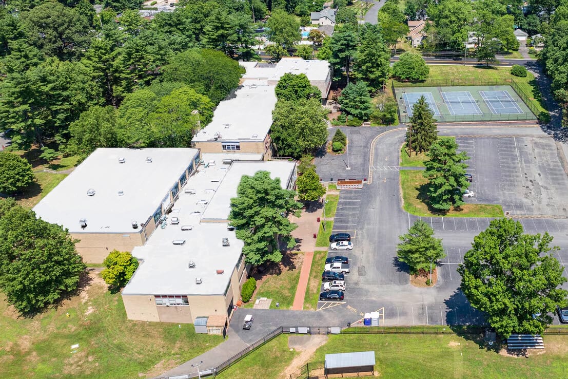 School campus aerial: multiple buildings, large parking lot, tennis courts, and green trees.