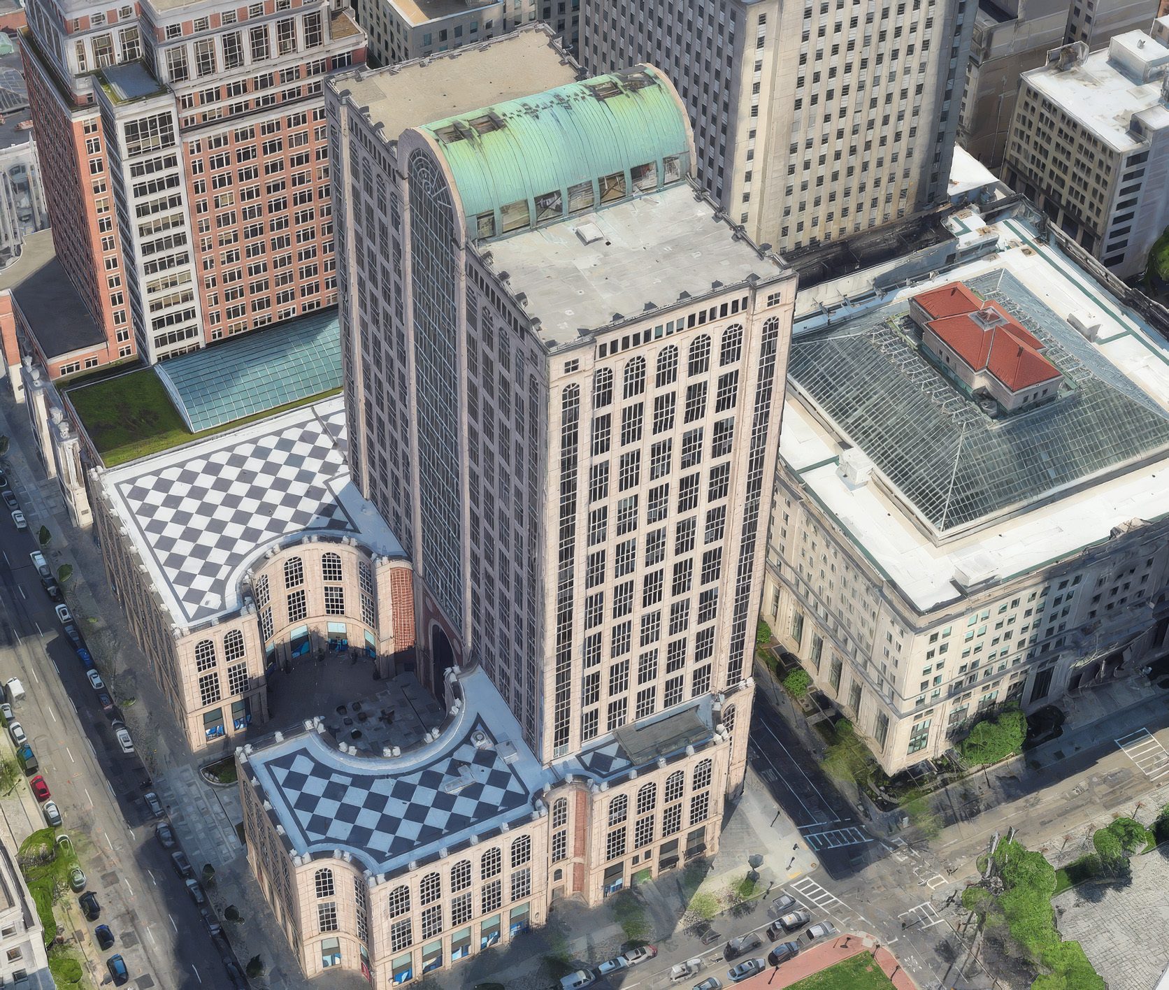 Aerial view of multiple large buildings, including a tall one with a green roof and checkerboard patterns.