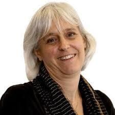 Smiling woman with short grey hair and a striped scarf, looking at the camera.