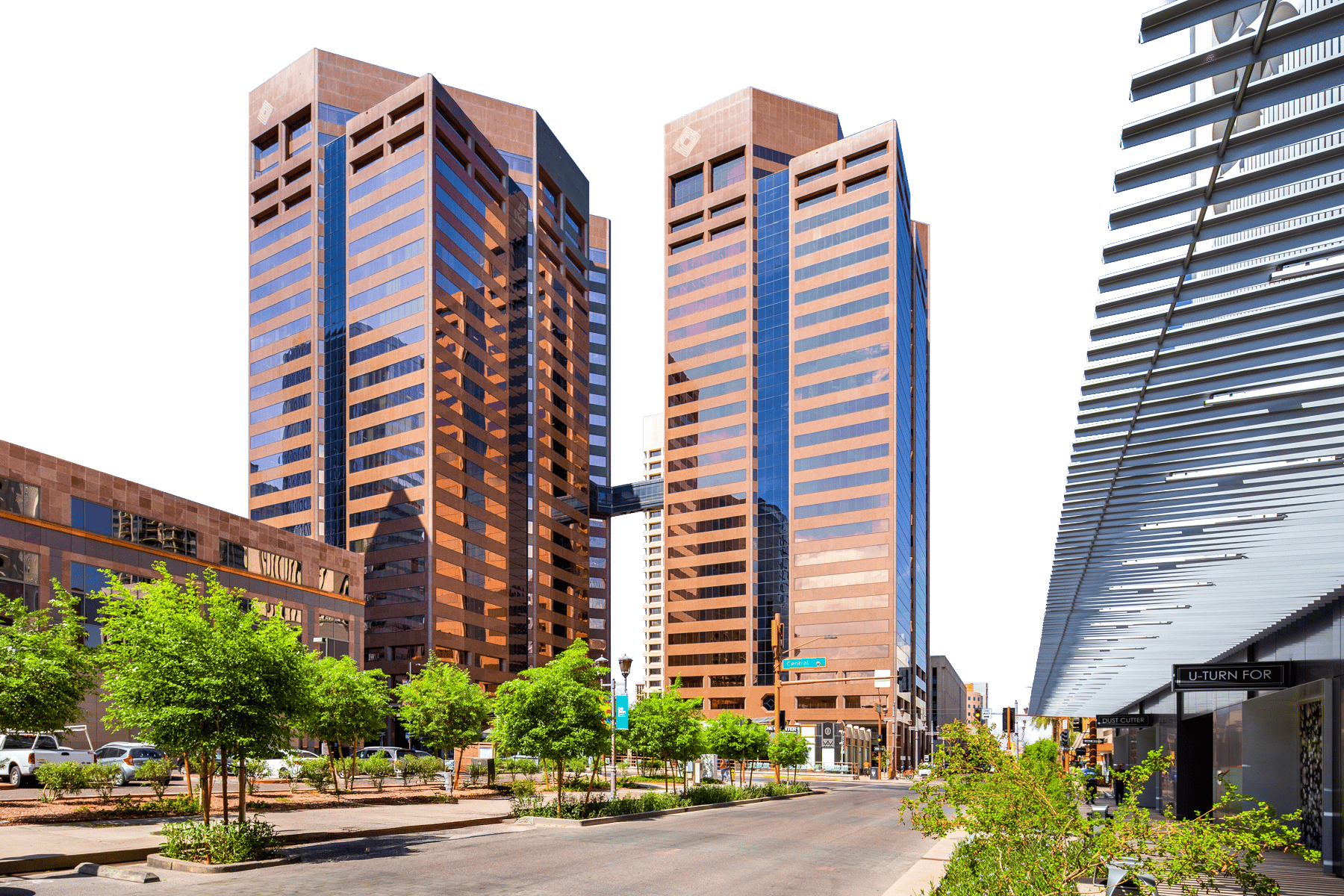 Modern city street scene featuring two tall brown and blue glass skyscrapers connected by a skywalk, with trees.