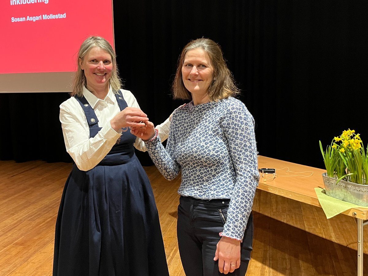 Two smiling women holding hands on stage in front of a presentation screen.