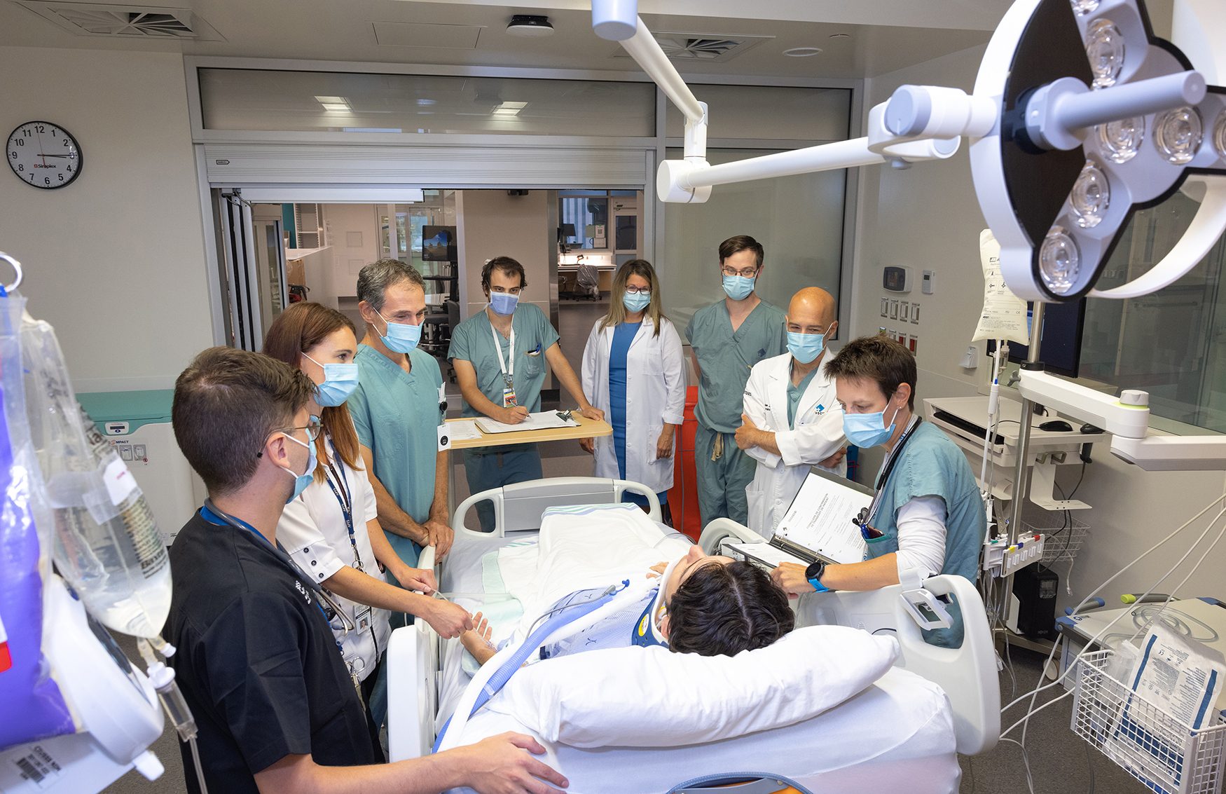 A team of medical professionals in masks surrounds a patient in a hospital bed, discussing the case.