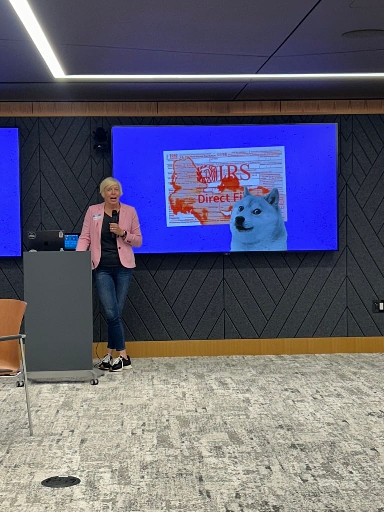 Woman speaks at podium; screen displays an IRS form, "Direct File," and Doge meme.