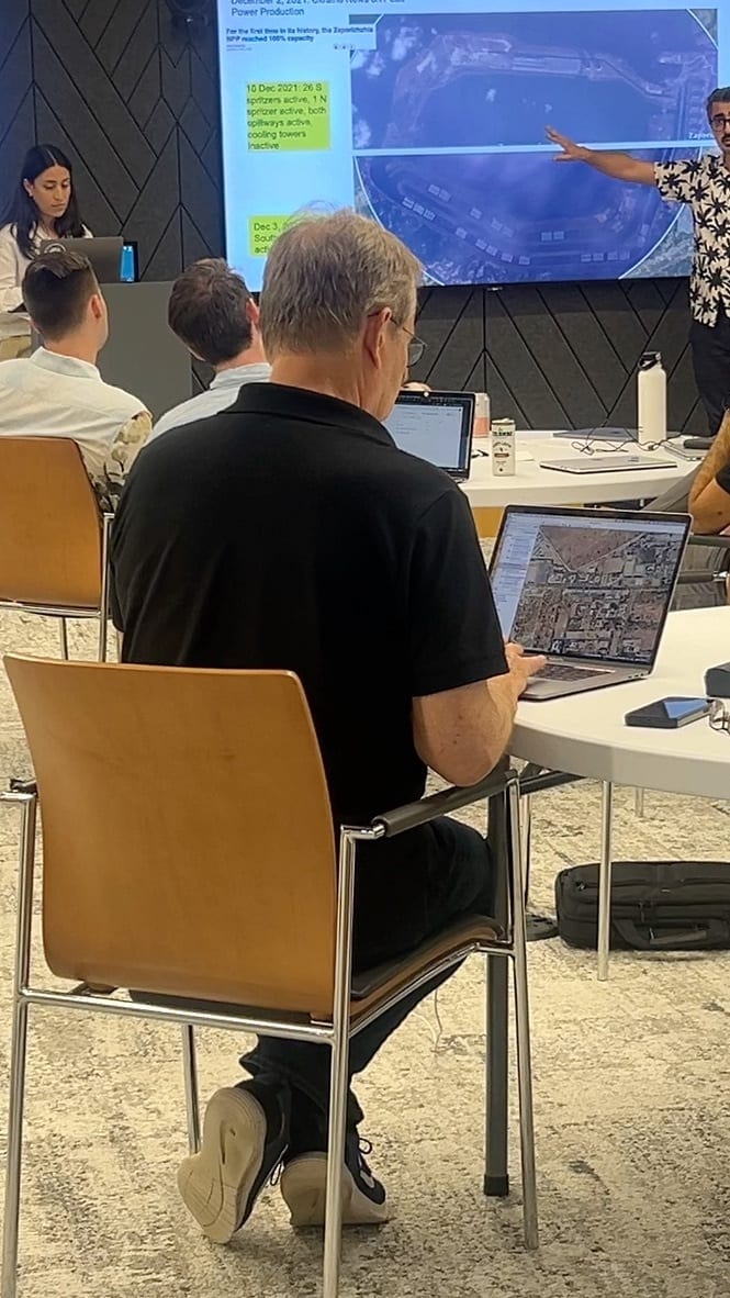 Man viewing satellite imagery on laptop during a presentation about a power plant.
