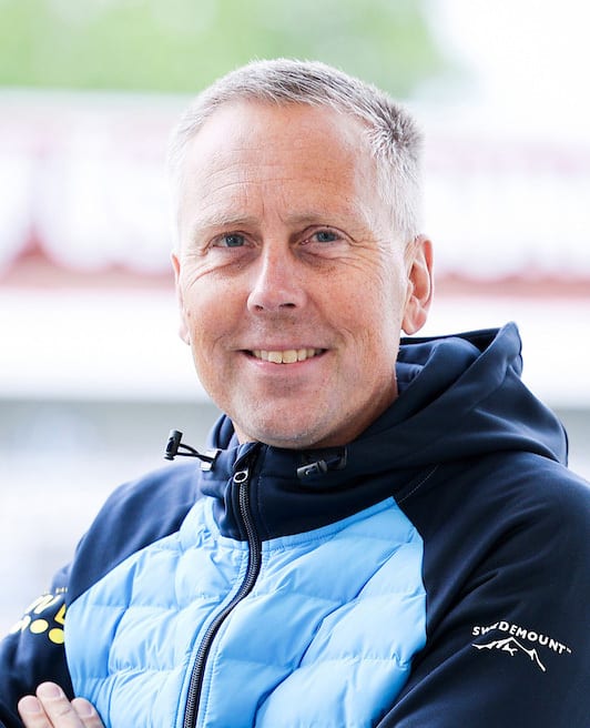 Smiling man with gray hair in a blue and black jacket, looking at the camera.