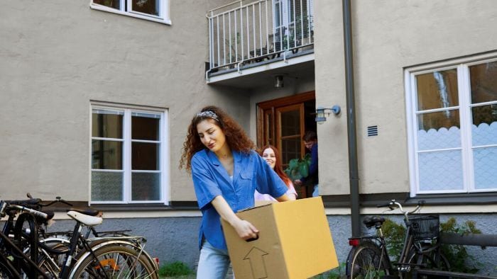 Friends moving into a new home, carrying boxes and a plant out of the entrance.
