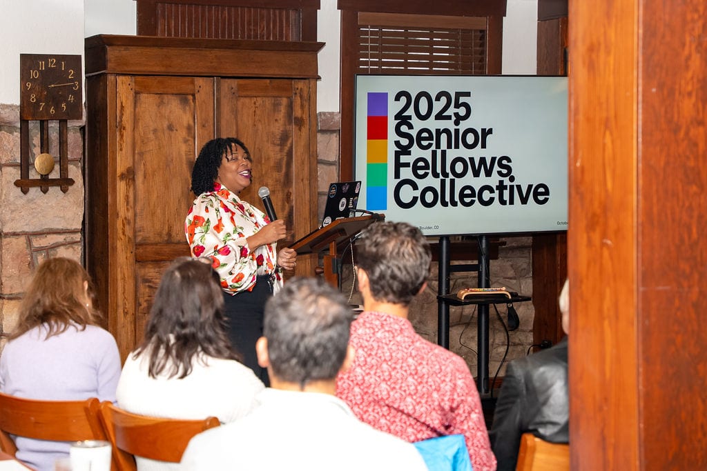 Woman presenting to an audience; screen shows "2025 Senior Fellows Collective".
