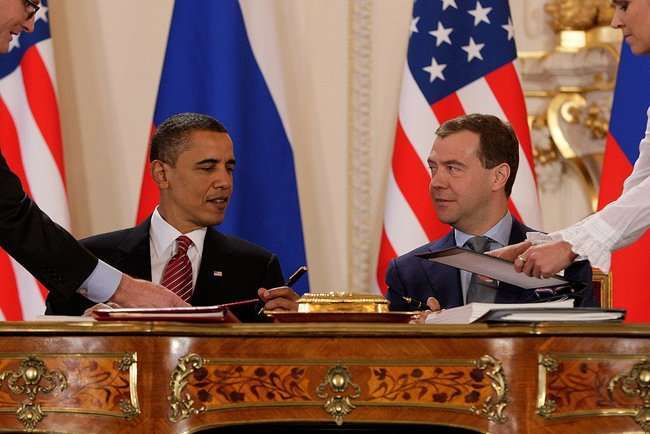 US President Obama and Russian President Medvedev signing documents at an ornate desk.