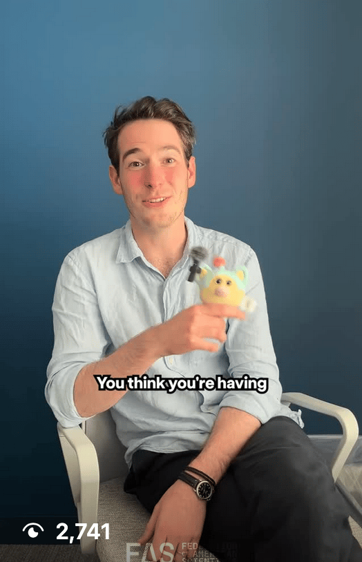 A smiling man sits, holding a small toy with a microphone.