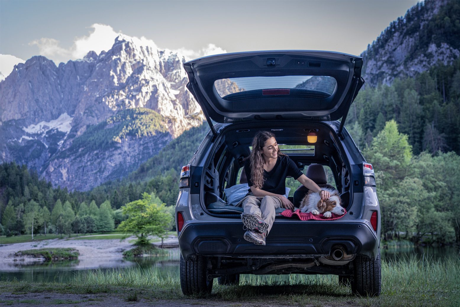 Woman, dog in SUV trunk by mountain lake.