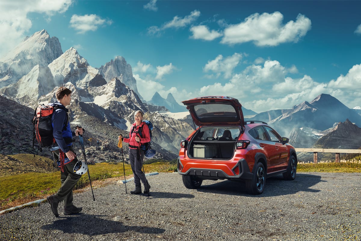 Two hikers next to a red SUV with open trunk at a mountain overlook.