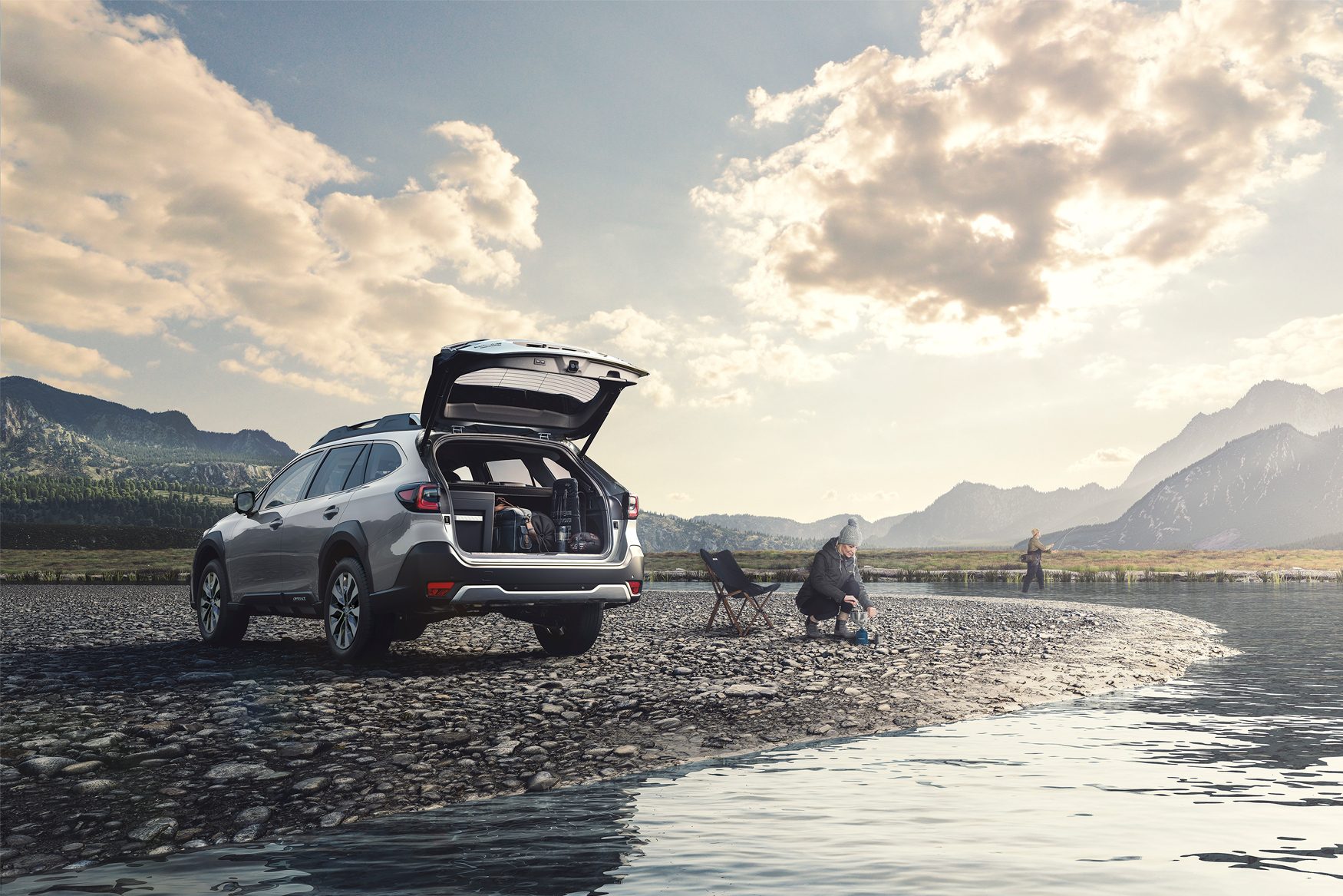 Car with open trunk on riverbank, person camping, person fishing, mountains in background.
