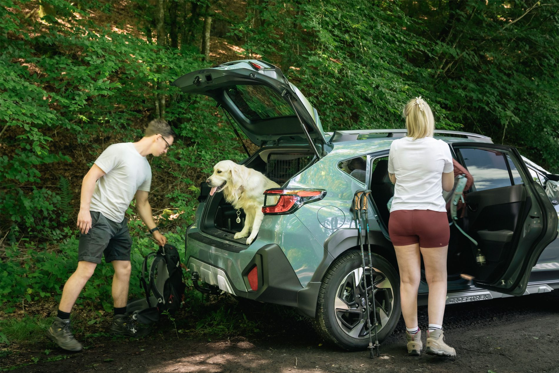 A couple and their dog by car loading gear for a hike in the woods.