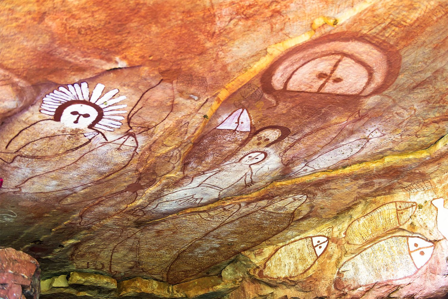 Rock art depicting various figures including humans, spirits, and fish on a textured cave ceiling.