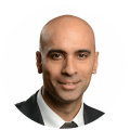 A bald man with a dark suit and tie smiles confidently at the camera in a professional headshot.