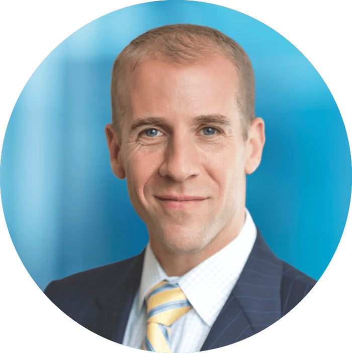 Headshot of a smiling man in a pinstripe suit and yellow-striped tie against a blue background.