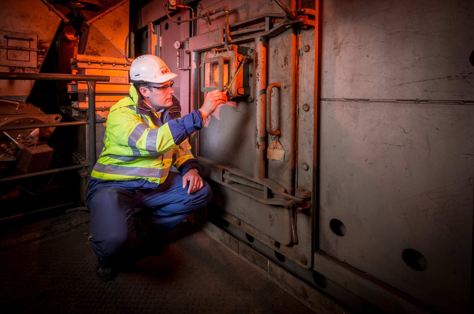 Worker in safety gear inspecting industrial machinery's viewport.