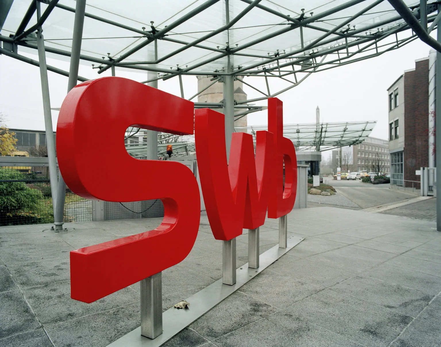 Large red "SWb" sign under a glass canopy, with buildings and a street in the background.