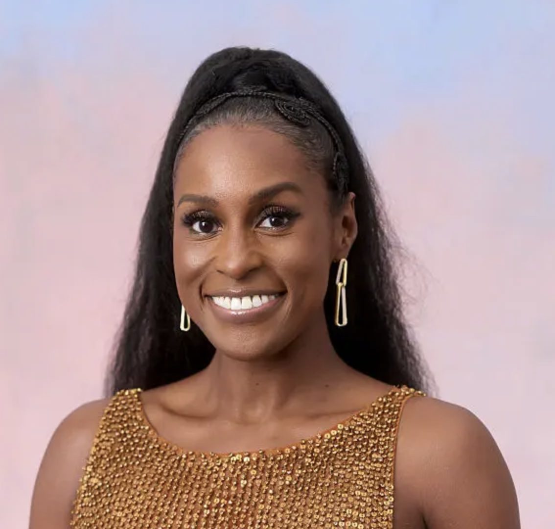 A smiling woman with dark hair in a high ponytail, wearing a gold sequined top, looking at the camera.
