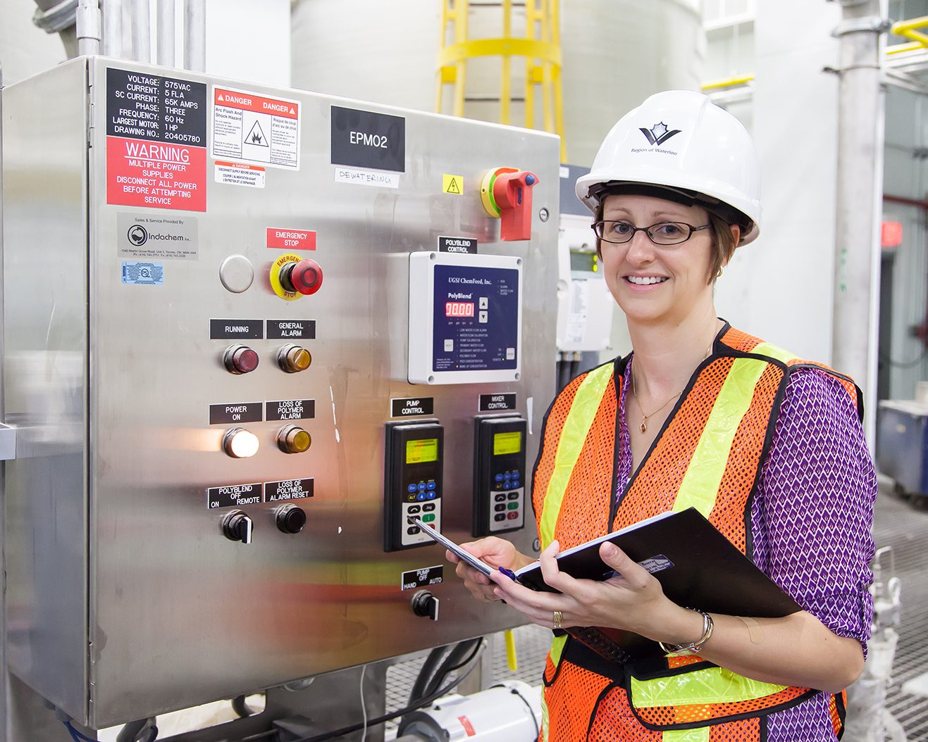 Staff person wearing a safety vest in front of a water treatment control panel. 