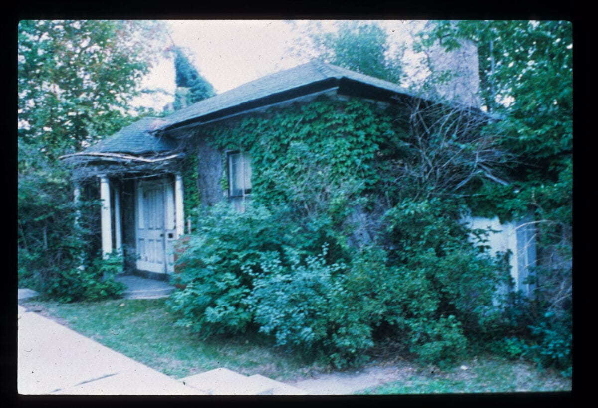 an image of McDougall Cottage prior to restoration. Vines are covering the building