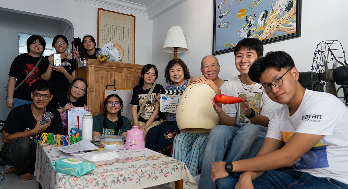 Smiling film crew and family with clapperboard and giant egg prop in a home.