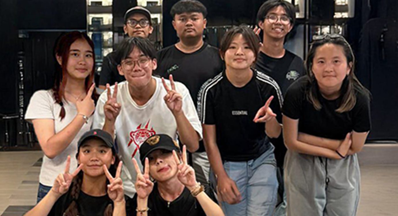 Nine young East Asian people posing for a photo, several making peace signs and smiling.