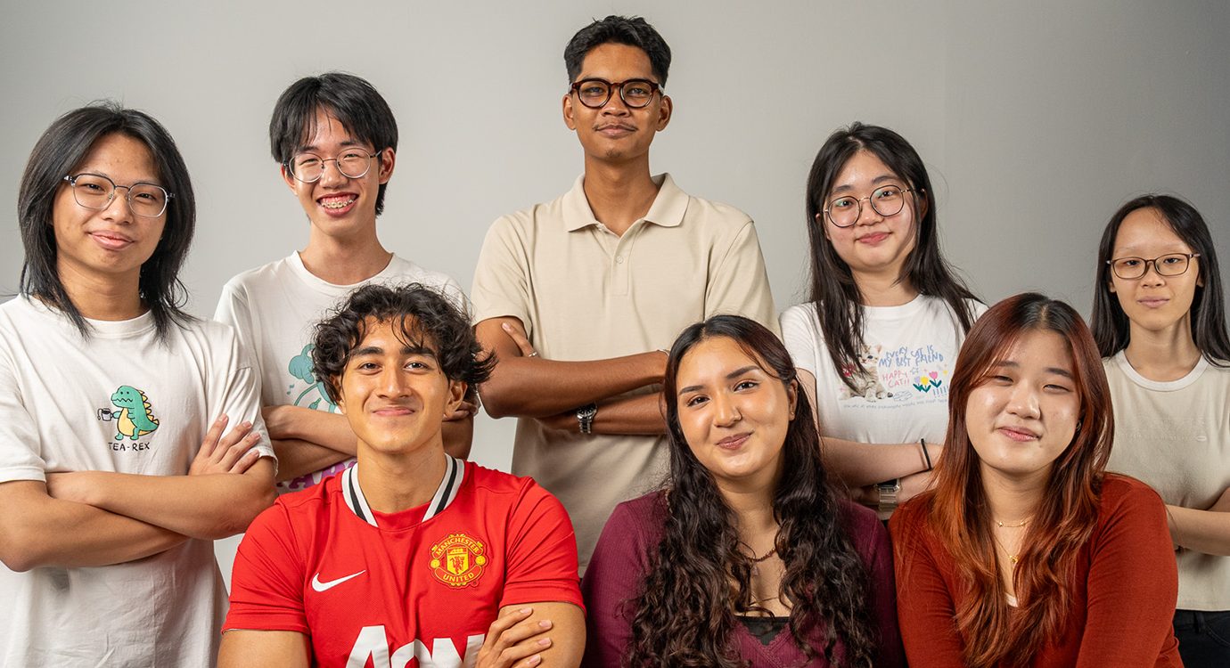 Group portrait of eight smiling young adults, some standing, some seated.