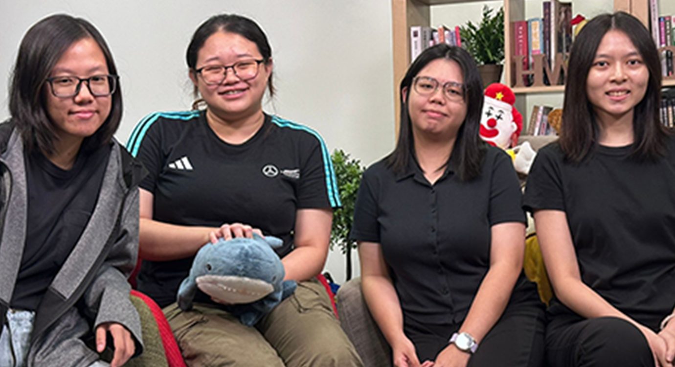 Four young Asian women, some smiling, seated indoors with a shark toy.